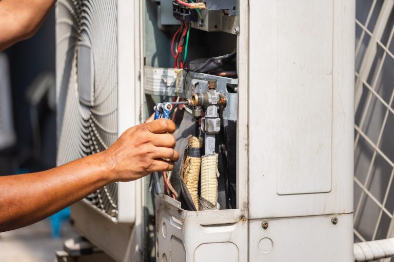 Technician performing maintenance service on home air conditioning system, Close up of hands using allen key to adjust valve on outdoor unit, HVAC contractor repairing a split system air conditioner