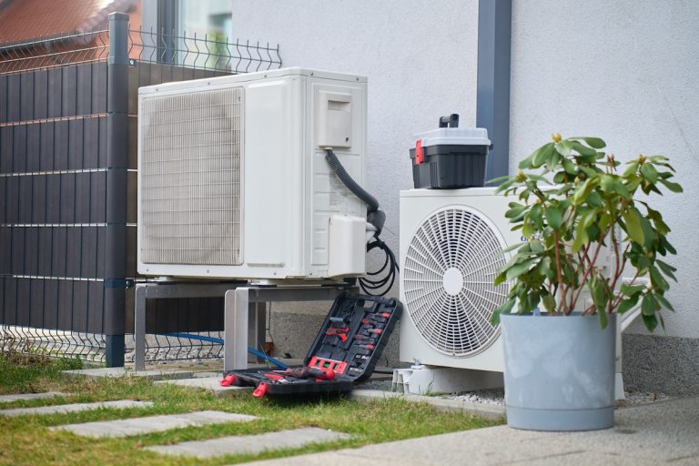 Outdoor heat pump units beside house with open toolbox and tools on ground.