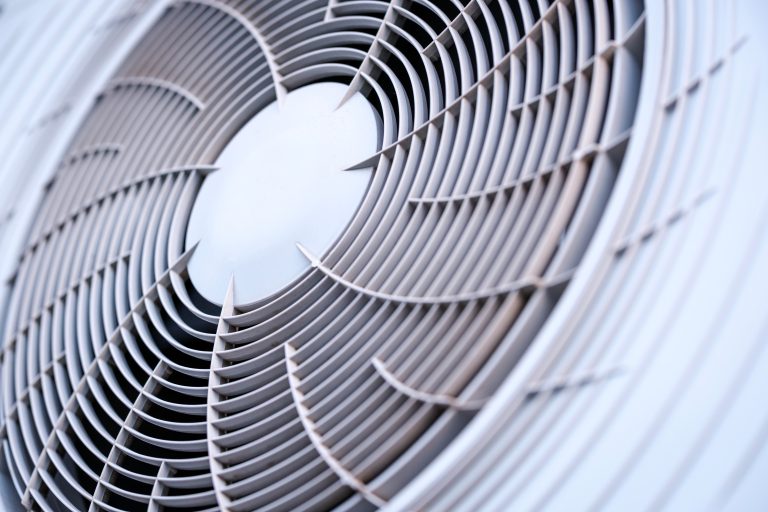 Fascinating abstract geometric pattern created by the circular gray plastic ventilation grille covering the rotating fan blades of a modern outdoor air conditioning unit