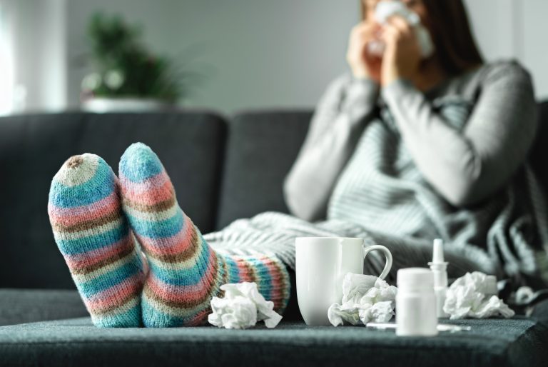Sick woman with flu, cold, fever and cough sitting on couch at h