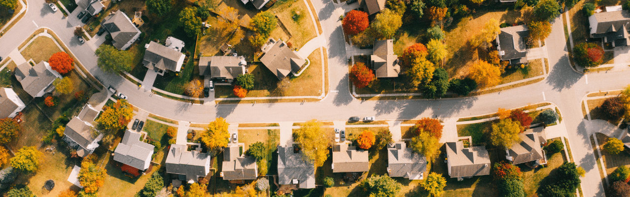 Aerial view of a suburban neighborhood with tree-lined streets and houses surrounded by colorful autumn foliage.