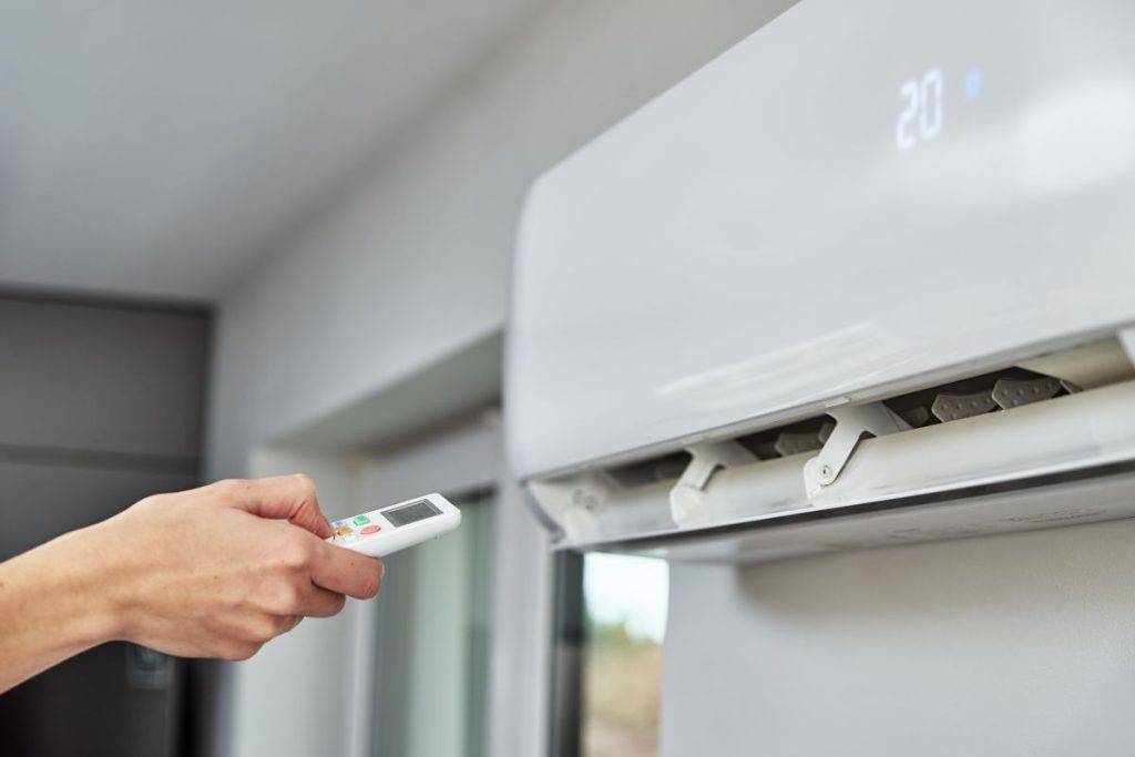 Hand adjusting temperature on air conditioner with remote control, Working air conditioner for comfort temperature in home during hot summer