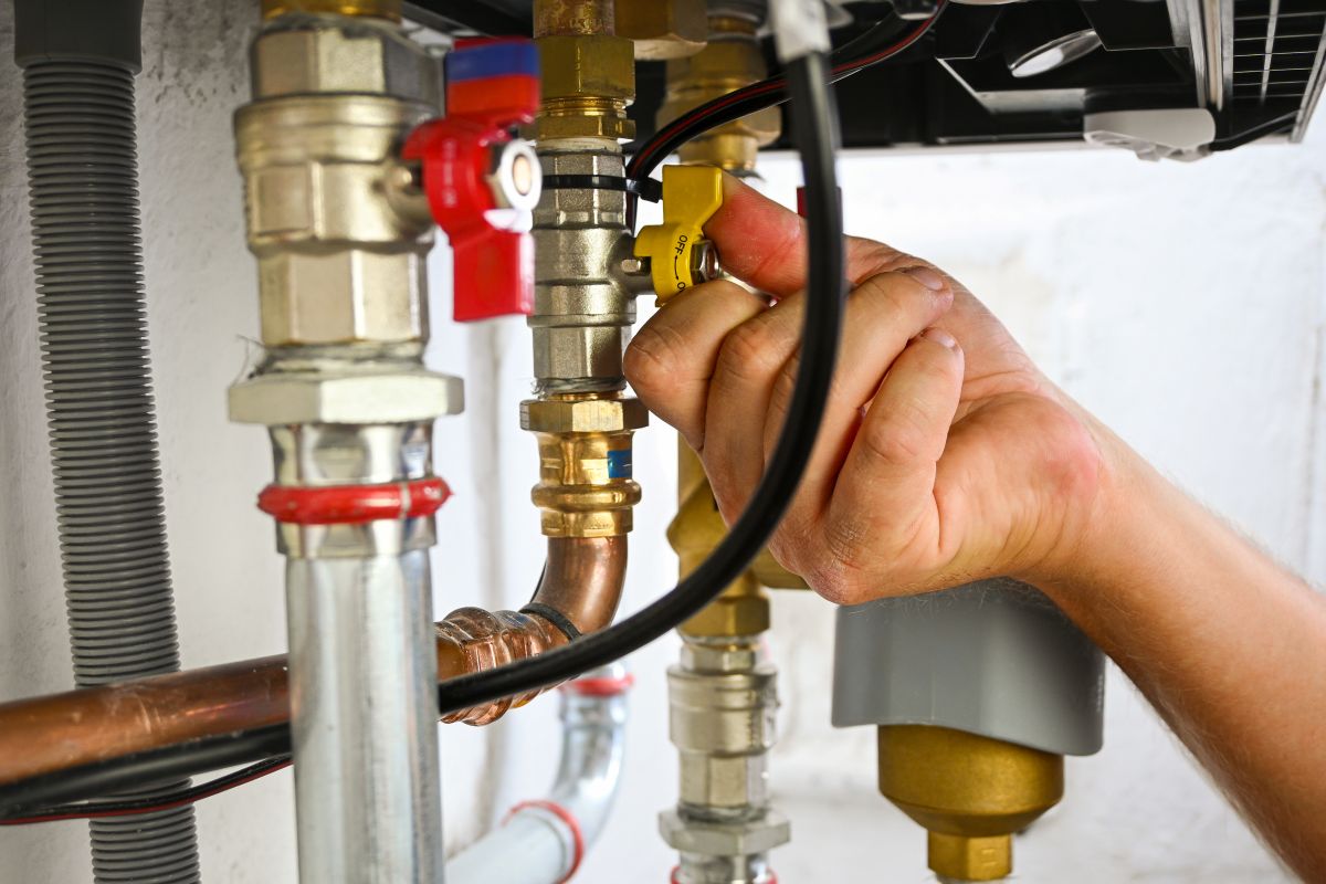 Hand turning a yellow valve on complex plumbing pipes in a boiler system