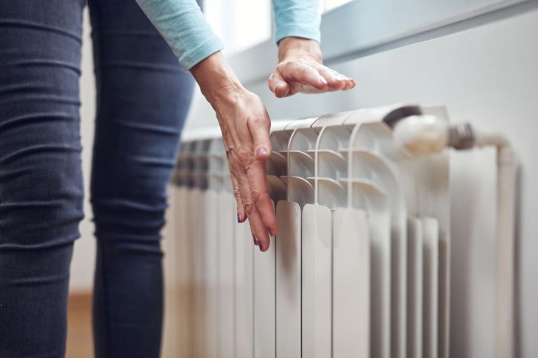 Woman heating her hands on the radiator during cold winter days.